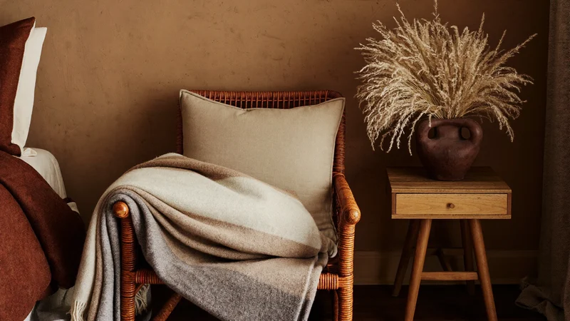 Angolo di camera con sedia in rattan, plaid piegato e brocca decorativa